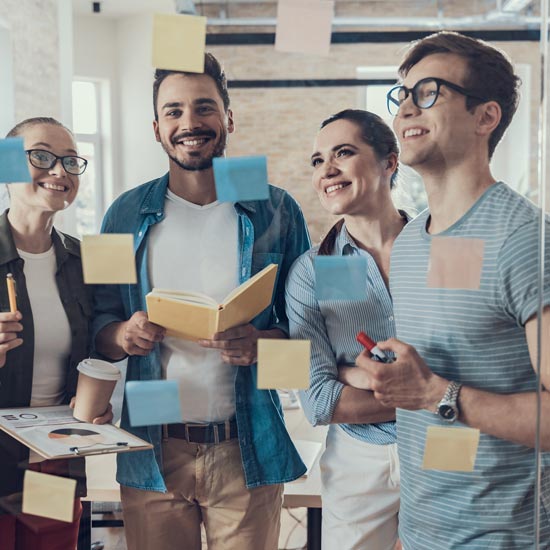 Starterkit für Start-ups: 5 Tipps für Gründer:innen Vier Personen stehen vor einer Glasscheibe mit Postits