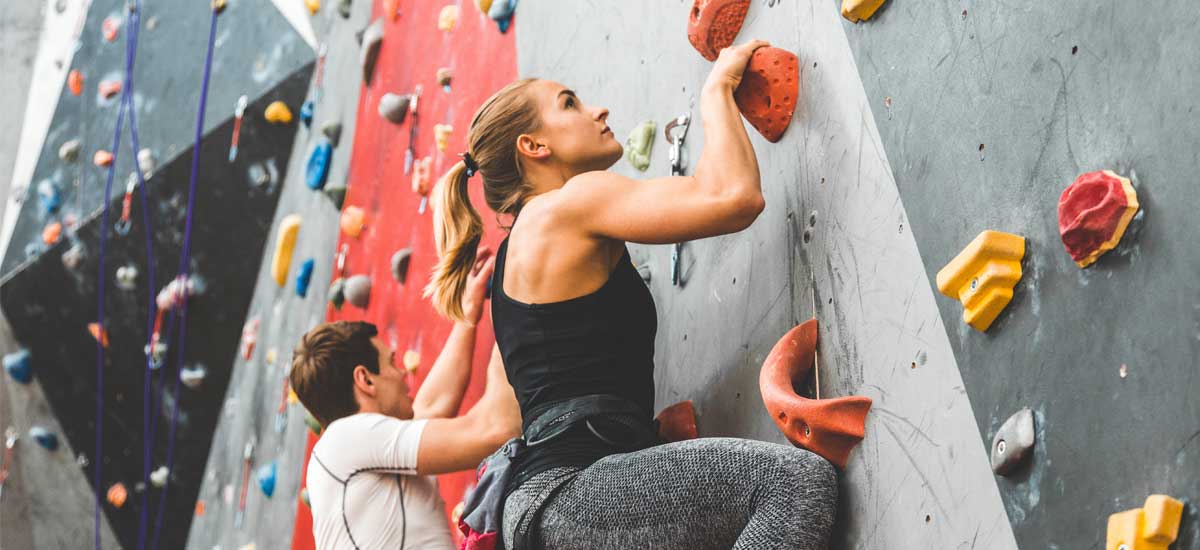 #1 Eine App für alle Fitnessstudios Eine Frau und ein Mann klettern eine Kletterwand hoch